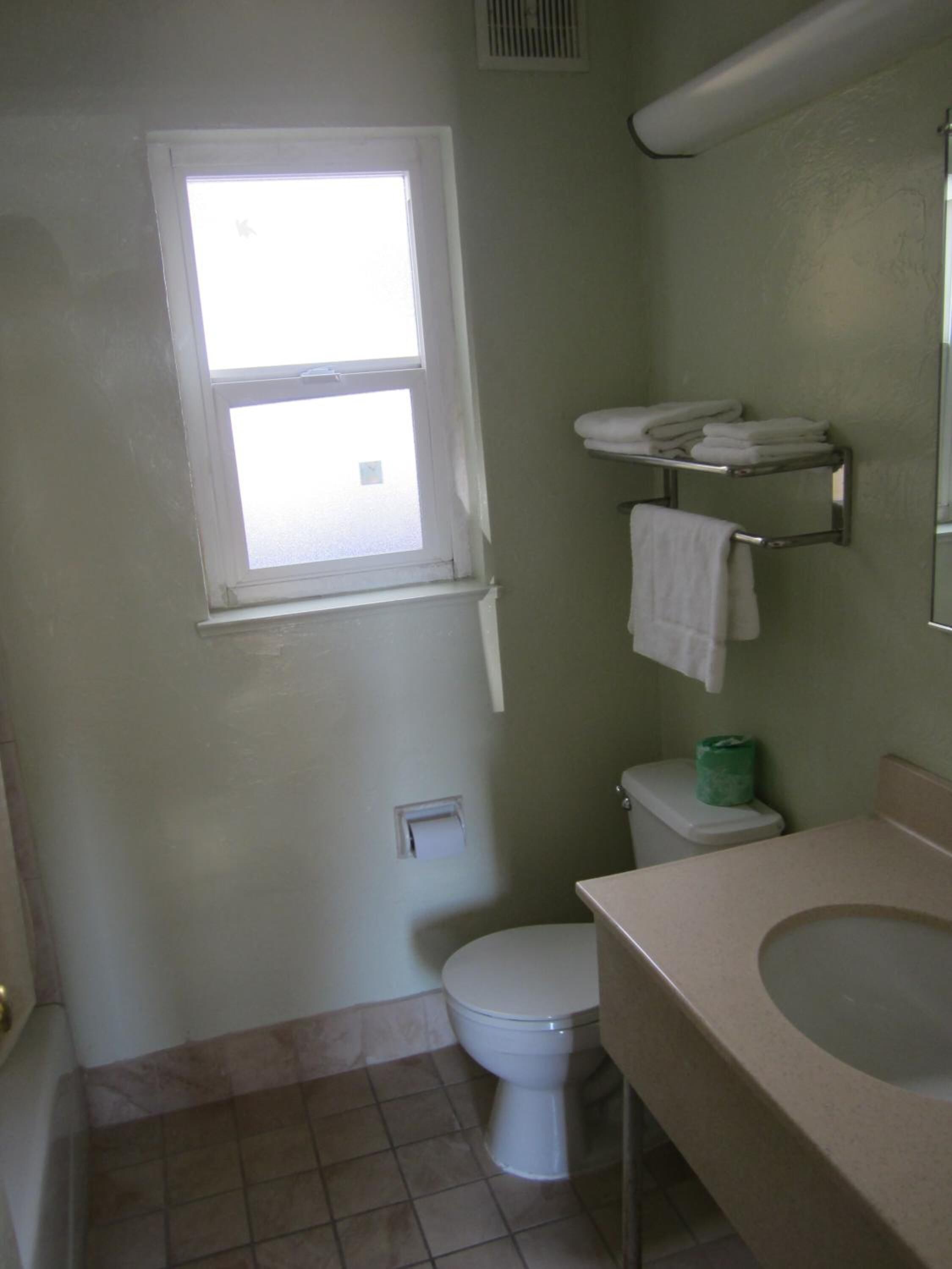 A bathroom with a toilet, a sink, a window, and a towel rack.