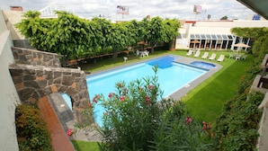 A swimming pool with a stone staircase leading up to a building, surrounded by greenery and a clear sky. - Hotel Real de Minas San Luis Potosi (San Luis Potosi)