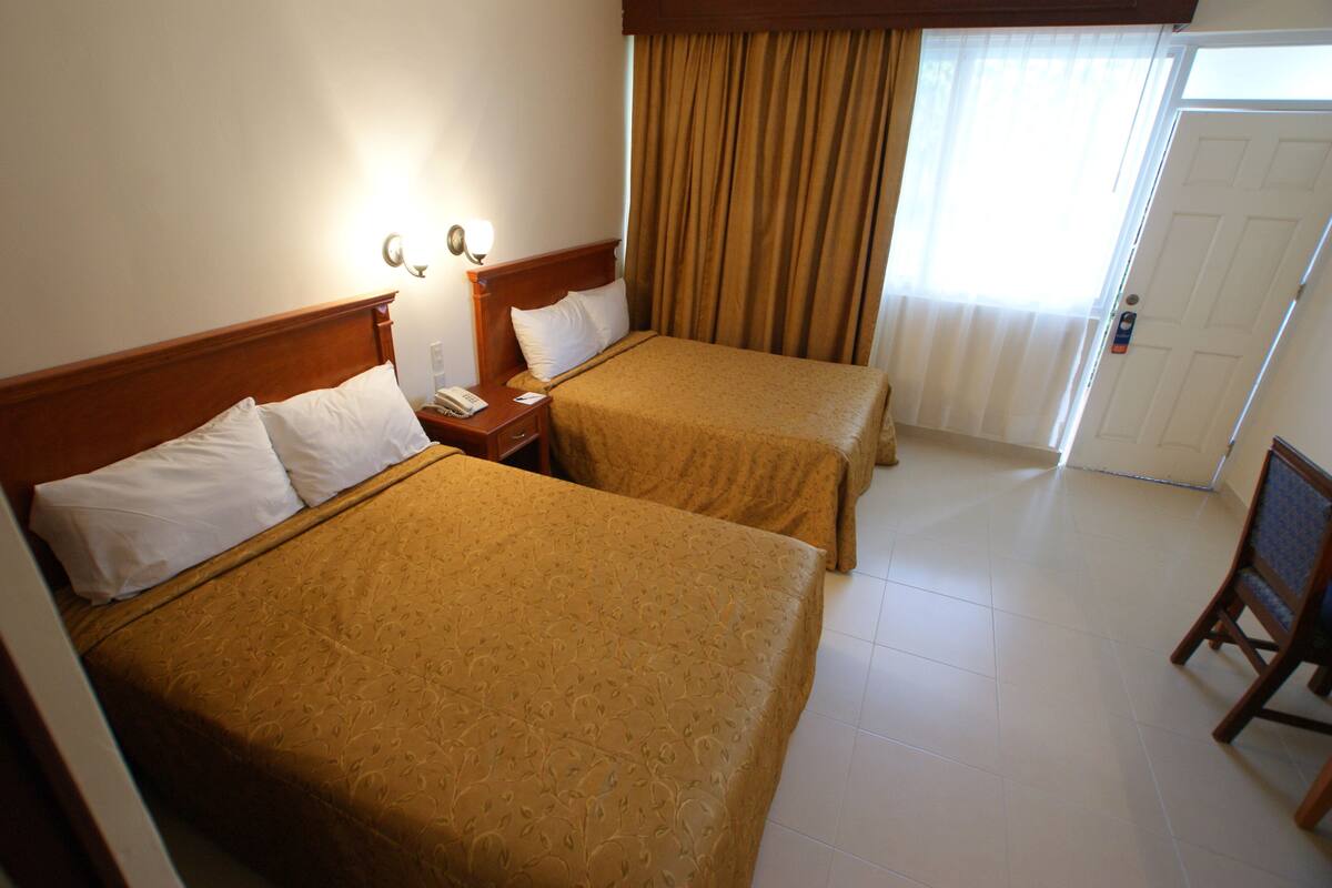 Quarto de hotel com duas camas, uma mesa de cabeceira, um telefone e uma cadeira.