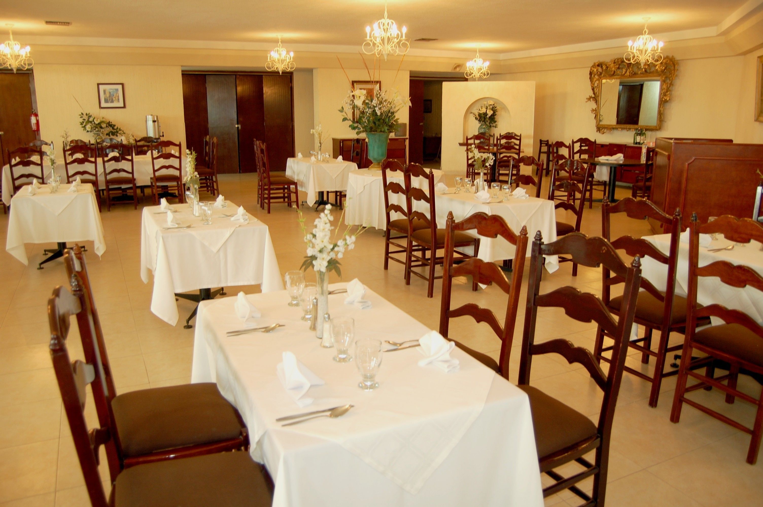 Un comedor con varias mesas dispuestas para el servicio, sillas de madera y candelabros.