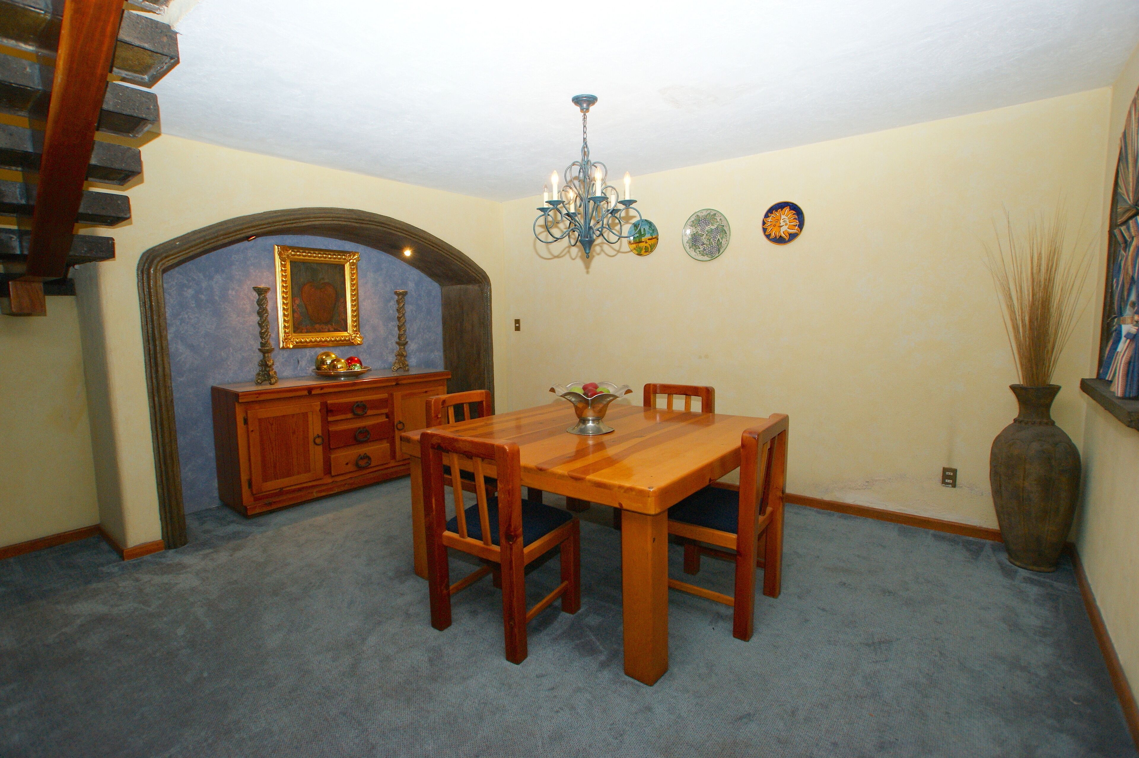 Un comedor con mesa y sillas de madera, una araña y un espejo decorativo.