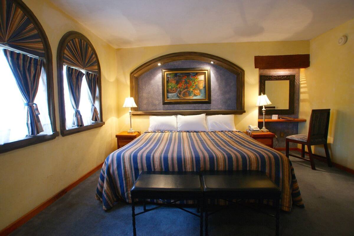 Quarto de hotel com cama grande, duas mesas de cabeceira, escrivaninha, cadeira e um quadro na parede.