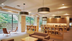 A modern library with bookshelves, seating areas, and large windows overlooking a garden. - Hakone Pax Yoshino (Hakone)