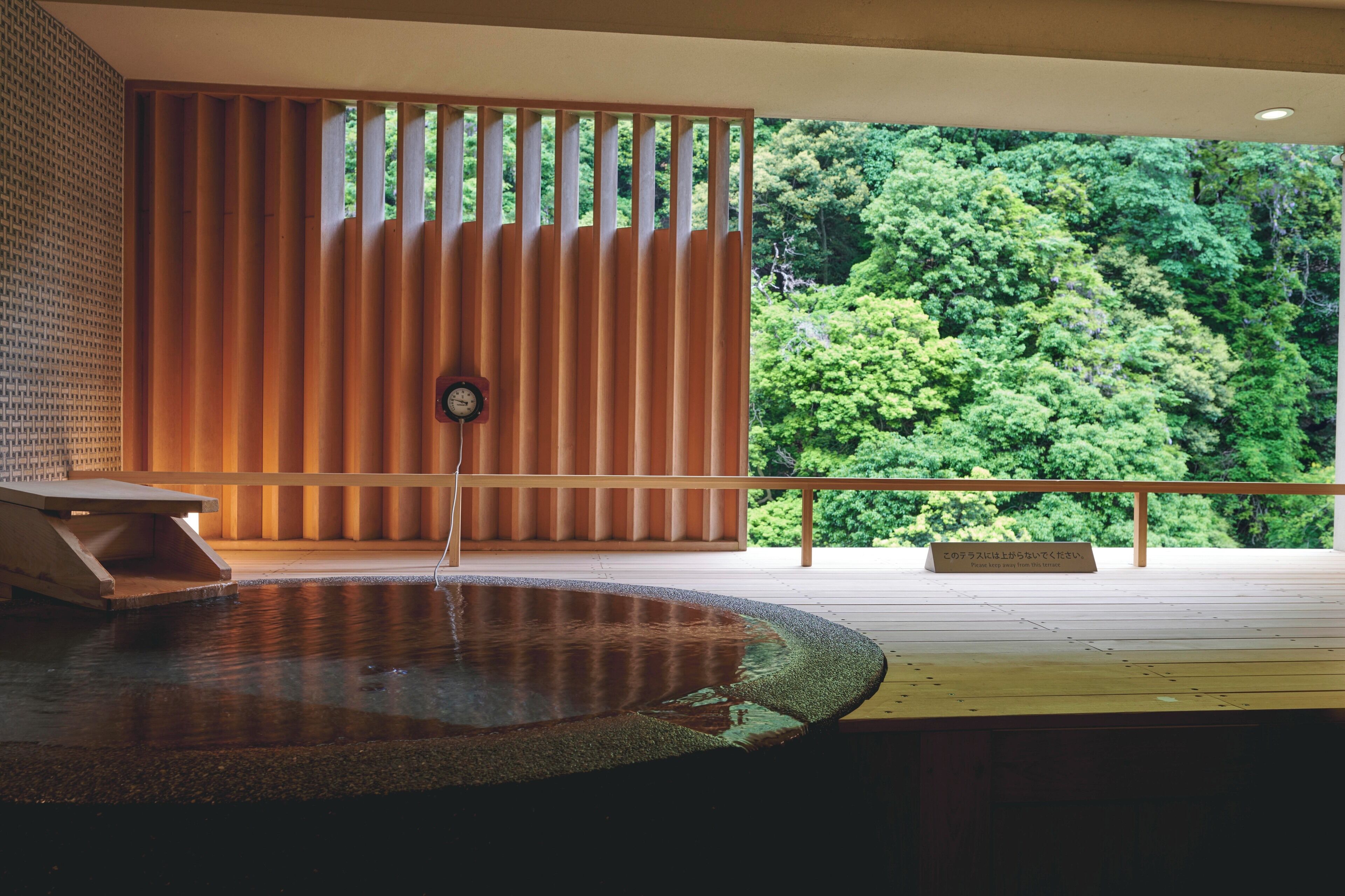 A wooden deck with a water feature, a wooden partition, and a view of a forest.
