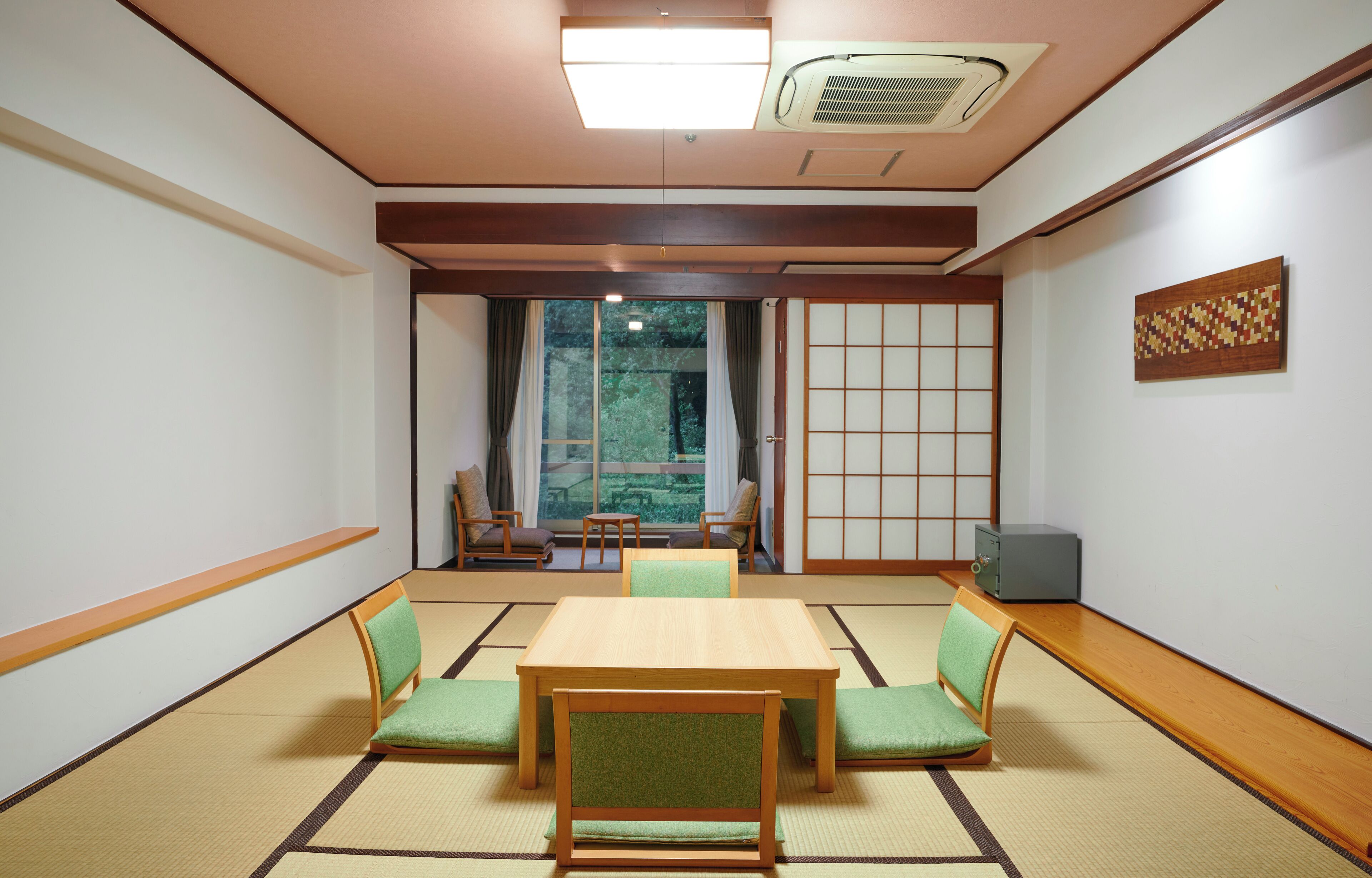 Una habitación tradicional japonesa con suelo de tatami, una mesa de madera baja y sillas con cojines verdes.
