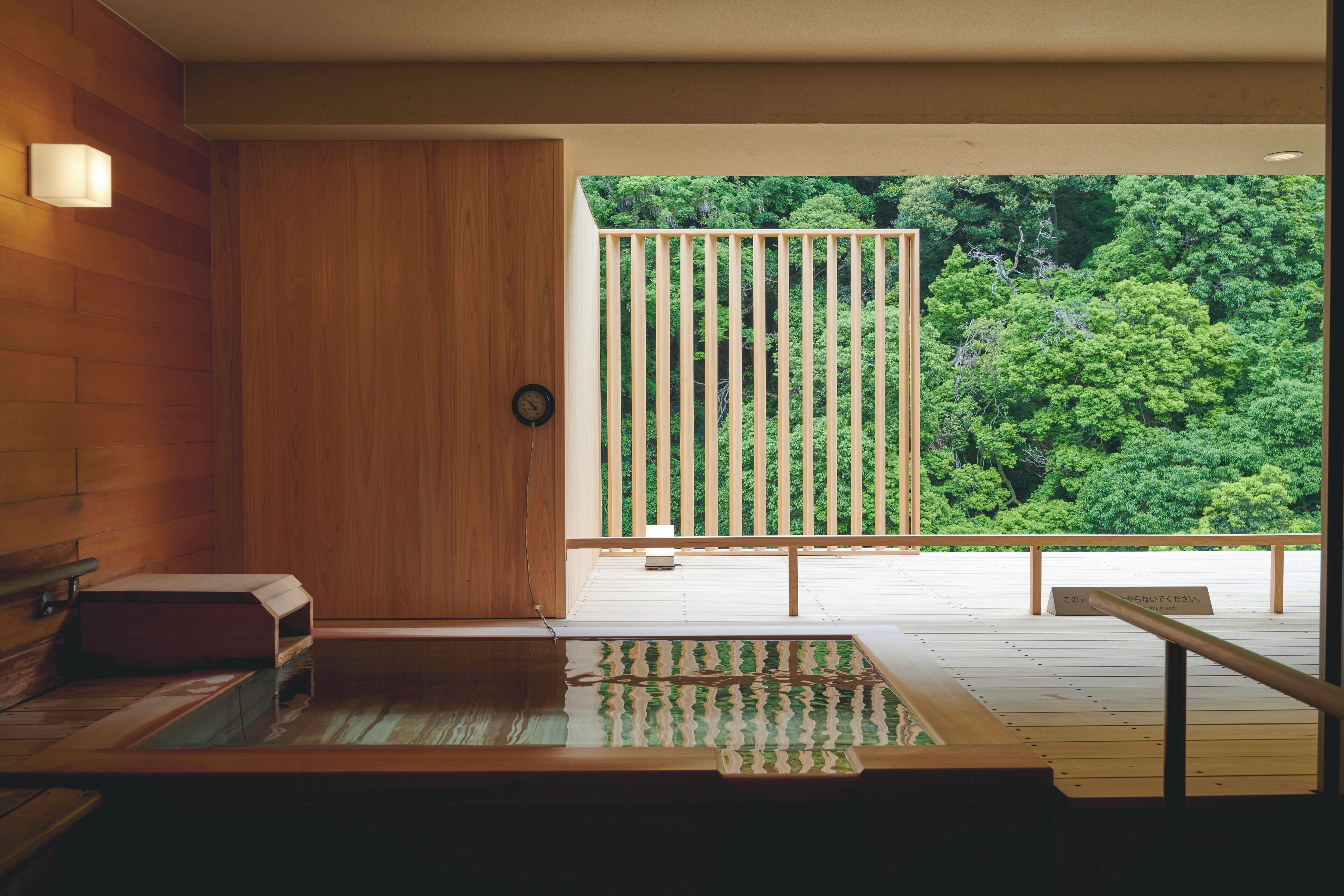 Un onsen japonais traditionnel, avec un intérieur en bois, un banc en bois et une vue sur une végétation luxuriante.