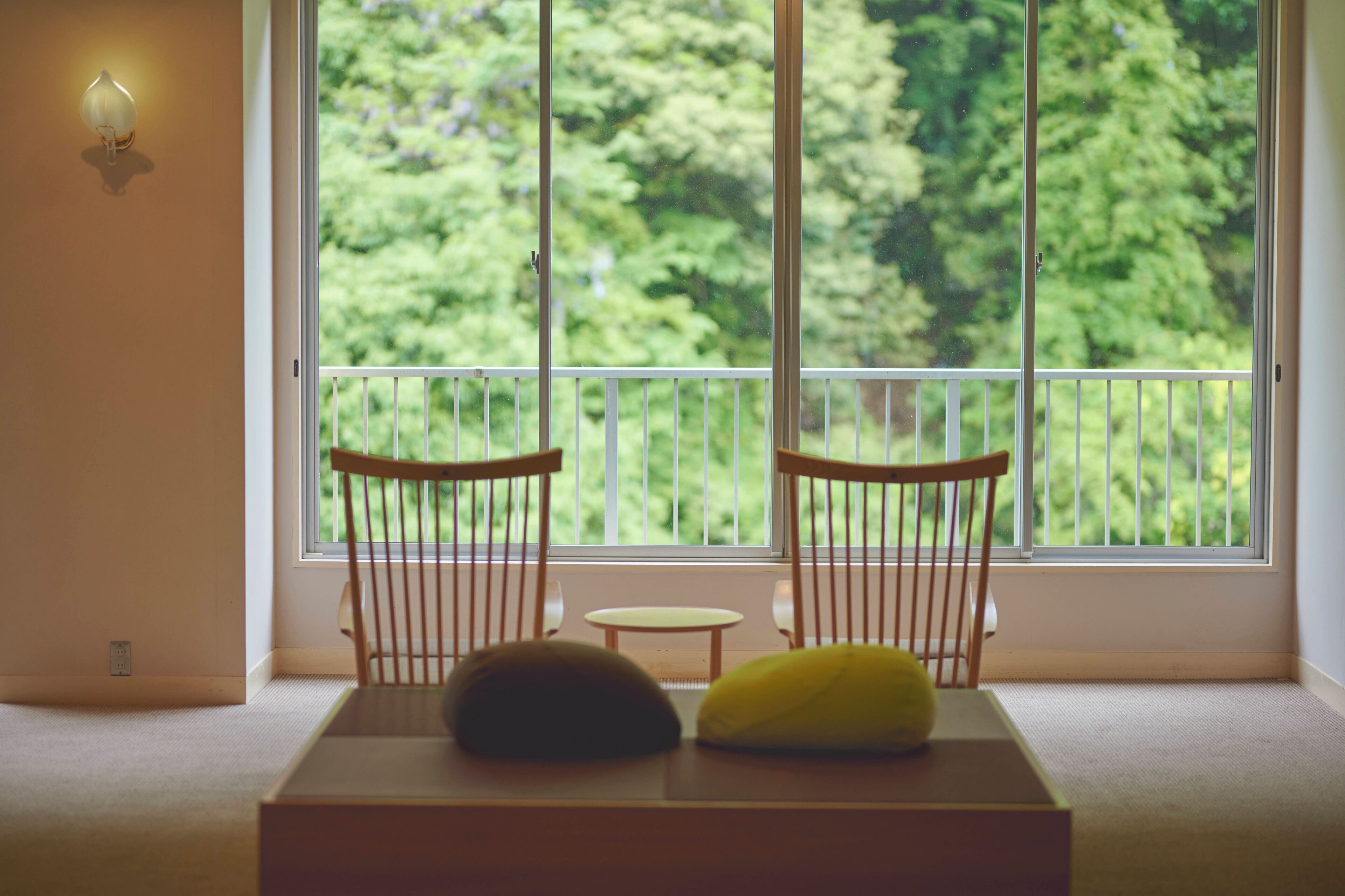 Une pièce avec une grande fenêtre, deux chaises en bois, une petite table ronde et un tapis beige.