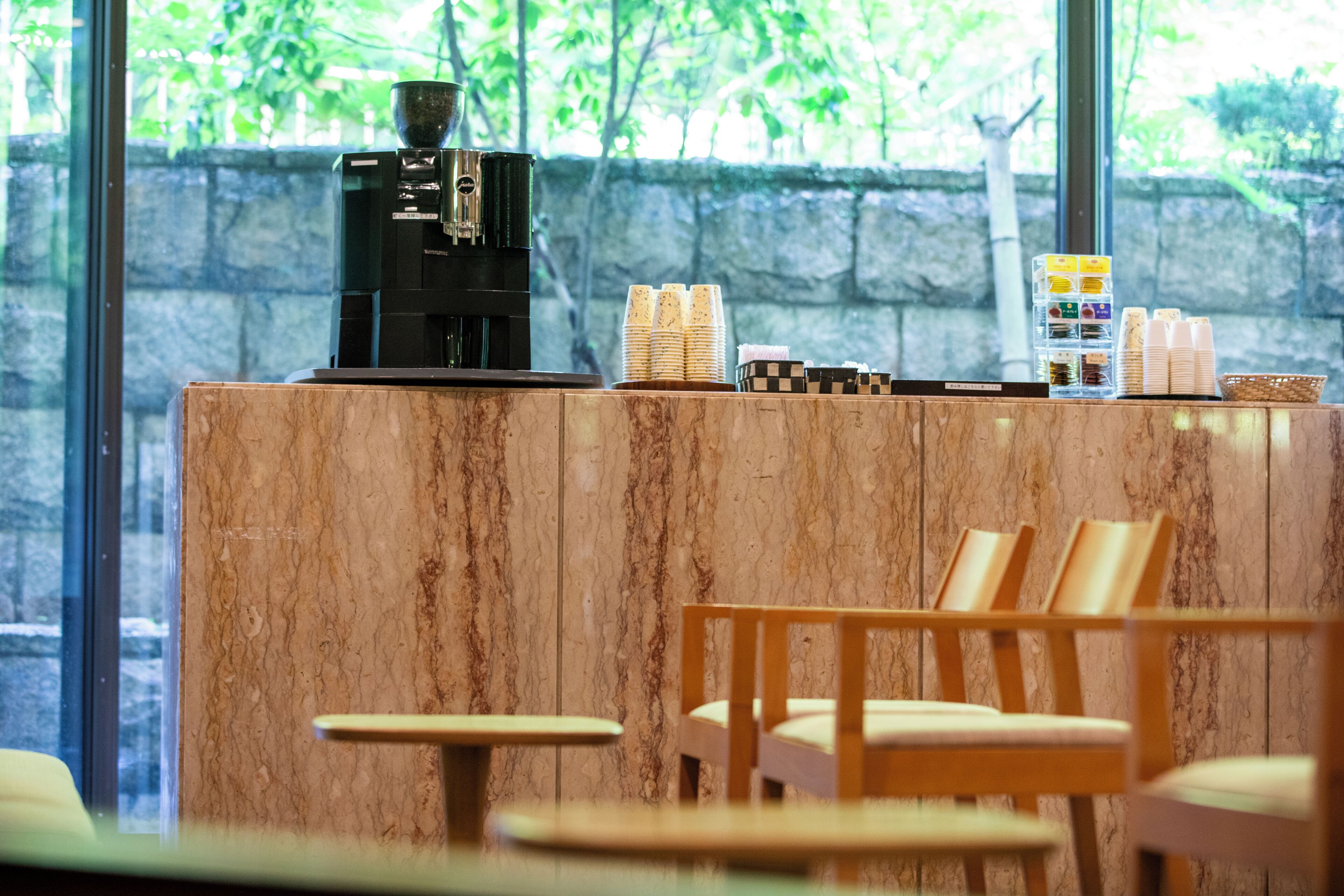 A coffee station with a coffee machine, stacked cups, and a basket of snacks.