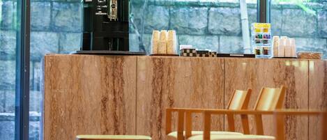 A coffee station with a coffee machine, stacked cups, and a basket of snacks.