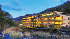 A multi-story hotel with balconies, located beside a river with visible rocks and vegetation. - Hakone Pax Yoshino (Hakone)