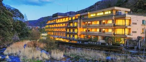 Ein mehrstöckiges Hotel mit Balkonen, gelegen am Flussufer mit sichtbaren Felsen und Vegetation.