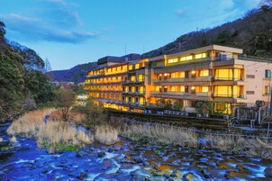 Un hotel de varios pisos con balcones, situado junto a un río con rocas y vegetación a la vista.