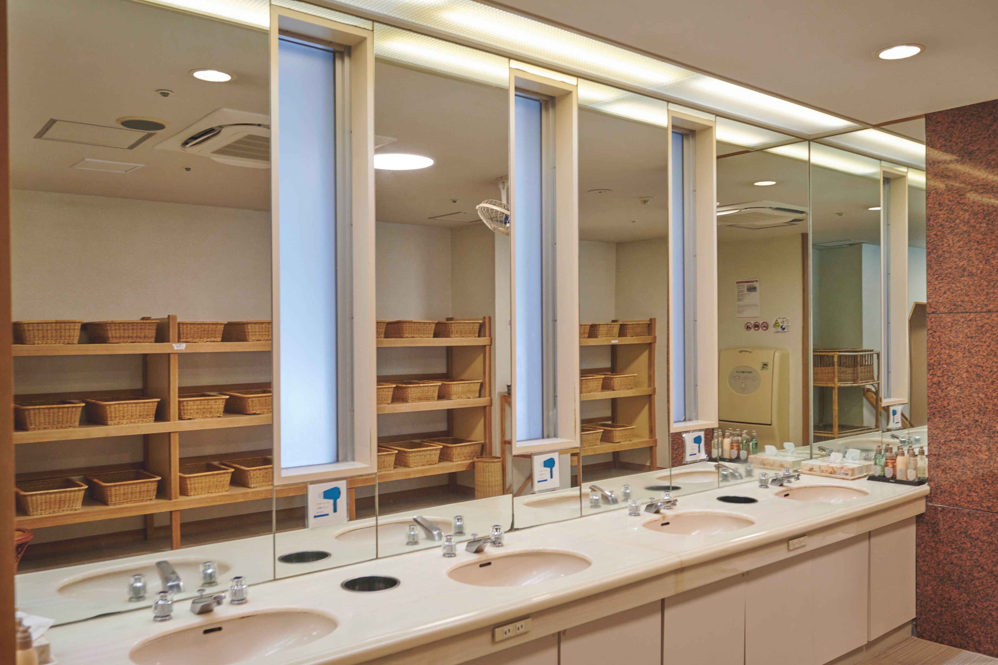 A long, modern bathroom with three sinks, wooden shelves with baskets, and a large mirror.