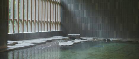 A traditional Japanese onsen with stone steps leading into a hot spring, a wooden fence, and a tiled wall.