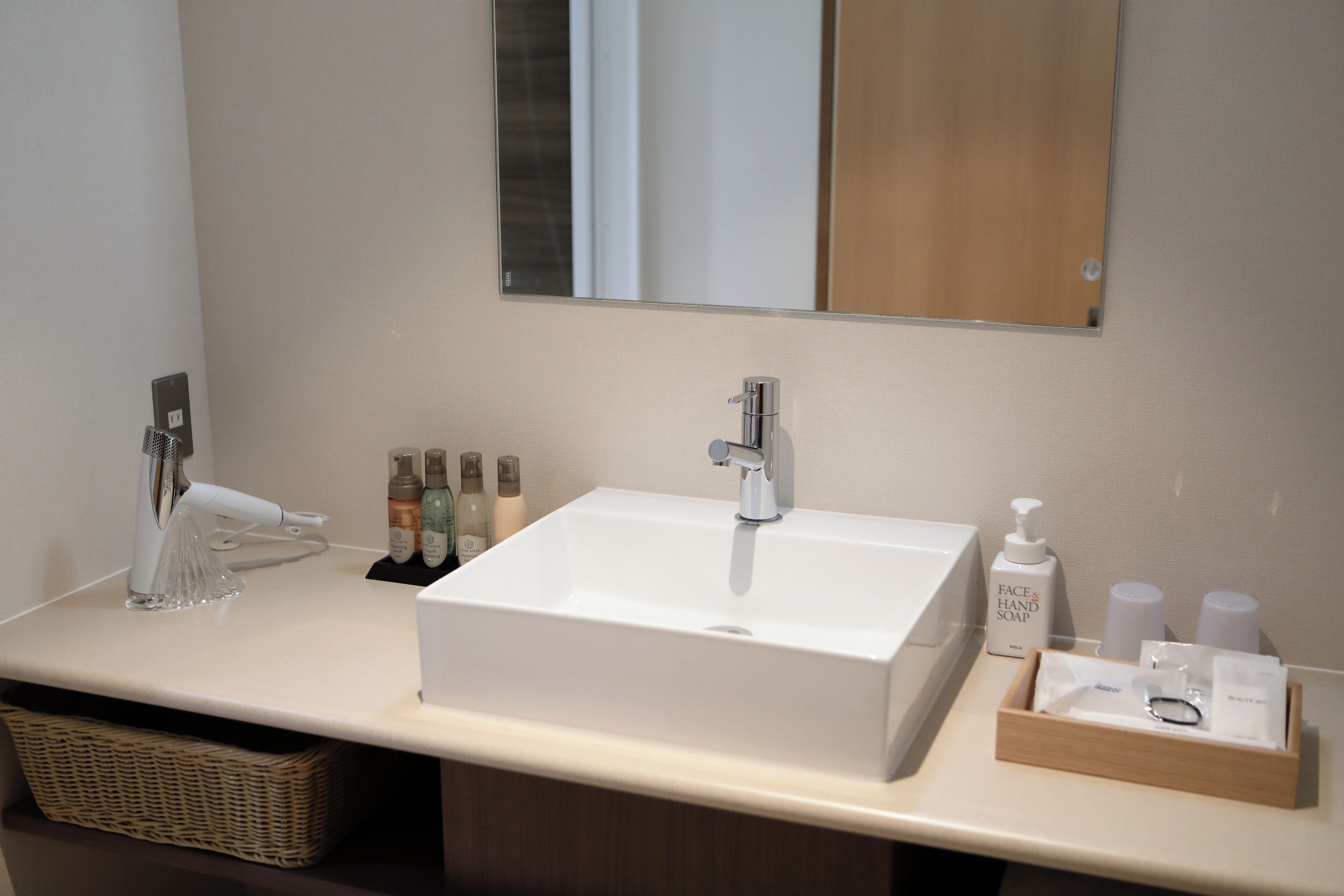 Une salle de bain moderne avec un grand lavabo blanc, un miroir au-dessus et des articles de toilette posés sur le comptoir.