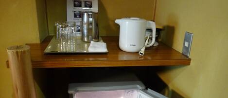 Een kleine keuken met een koelkast, waterkoker en koffiezetapparaat op een houten aanrecht.