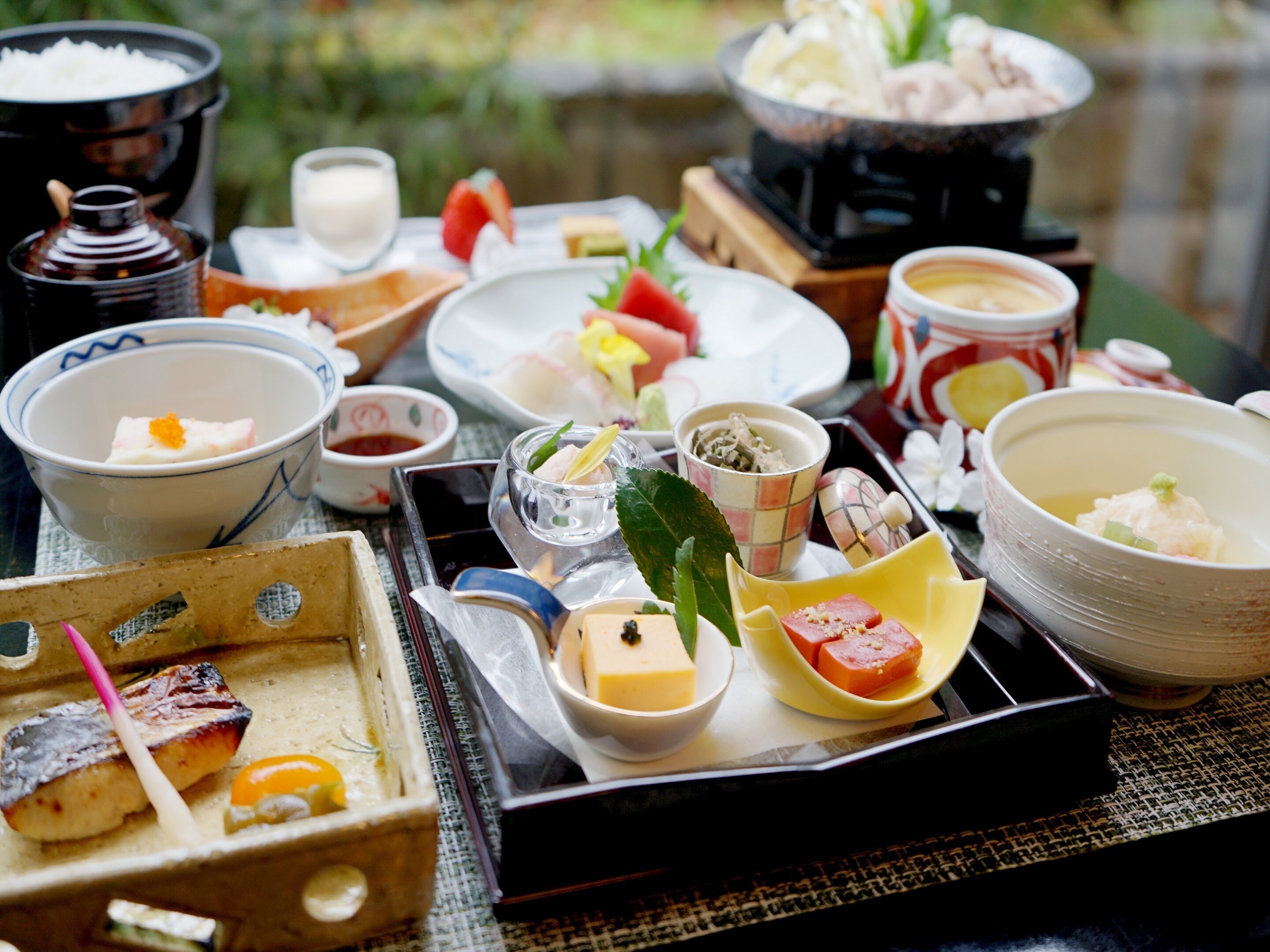 A variety of Japanese dishes including sushi, sashimi, and bowls of soup, arranged on a tray.