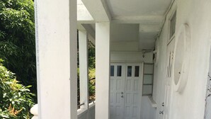 Un couloir étroit aux murs blancs et au sol carrelé, qui mène à une porte dotée d’une fenêtre.