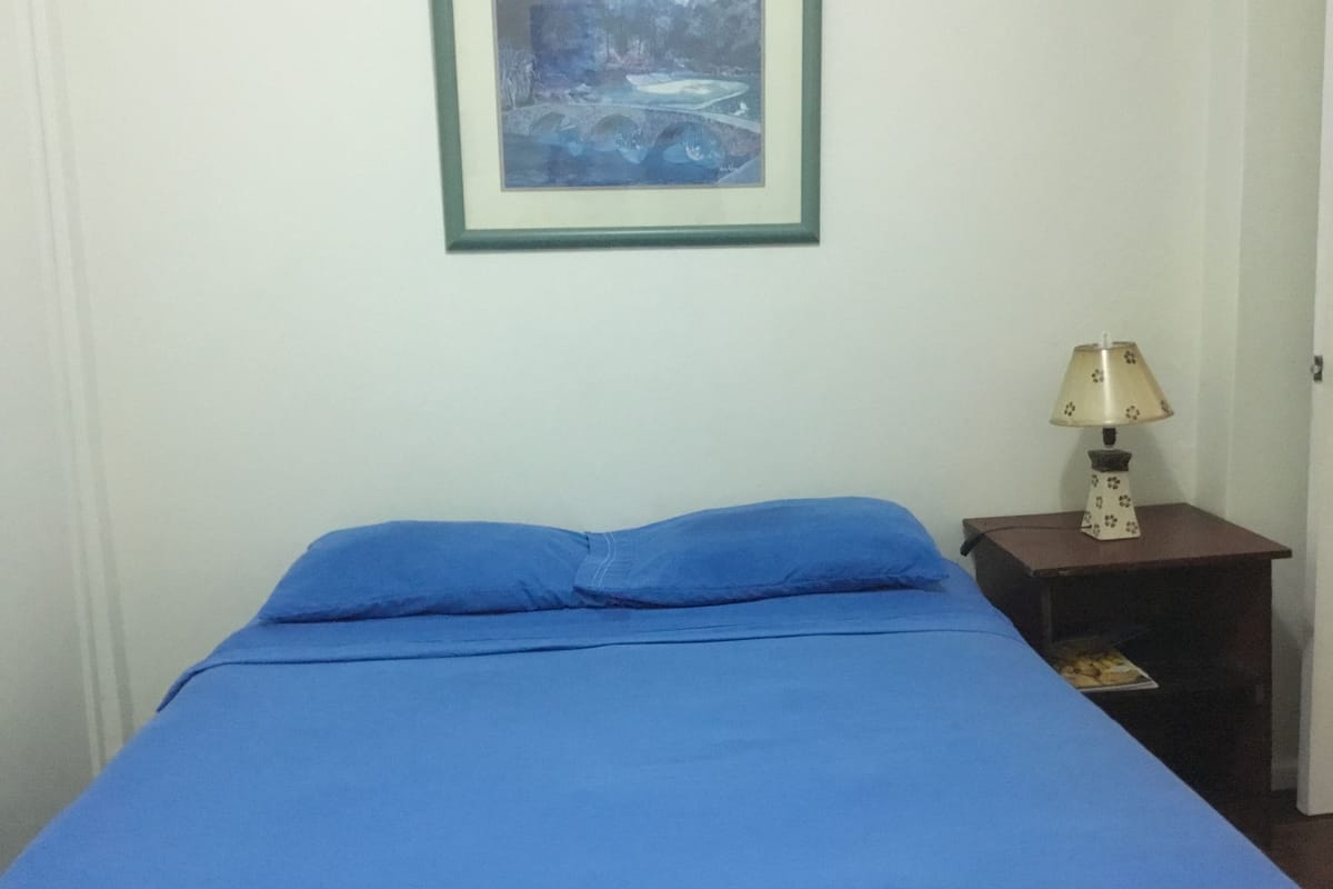 Une chambre avec un lit, un tableau encadré au mur et une table de chevet avec une lampe.