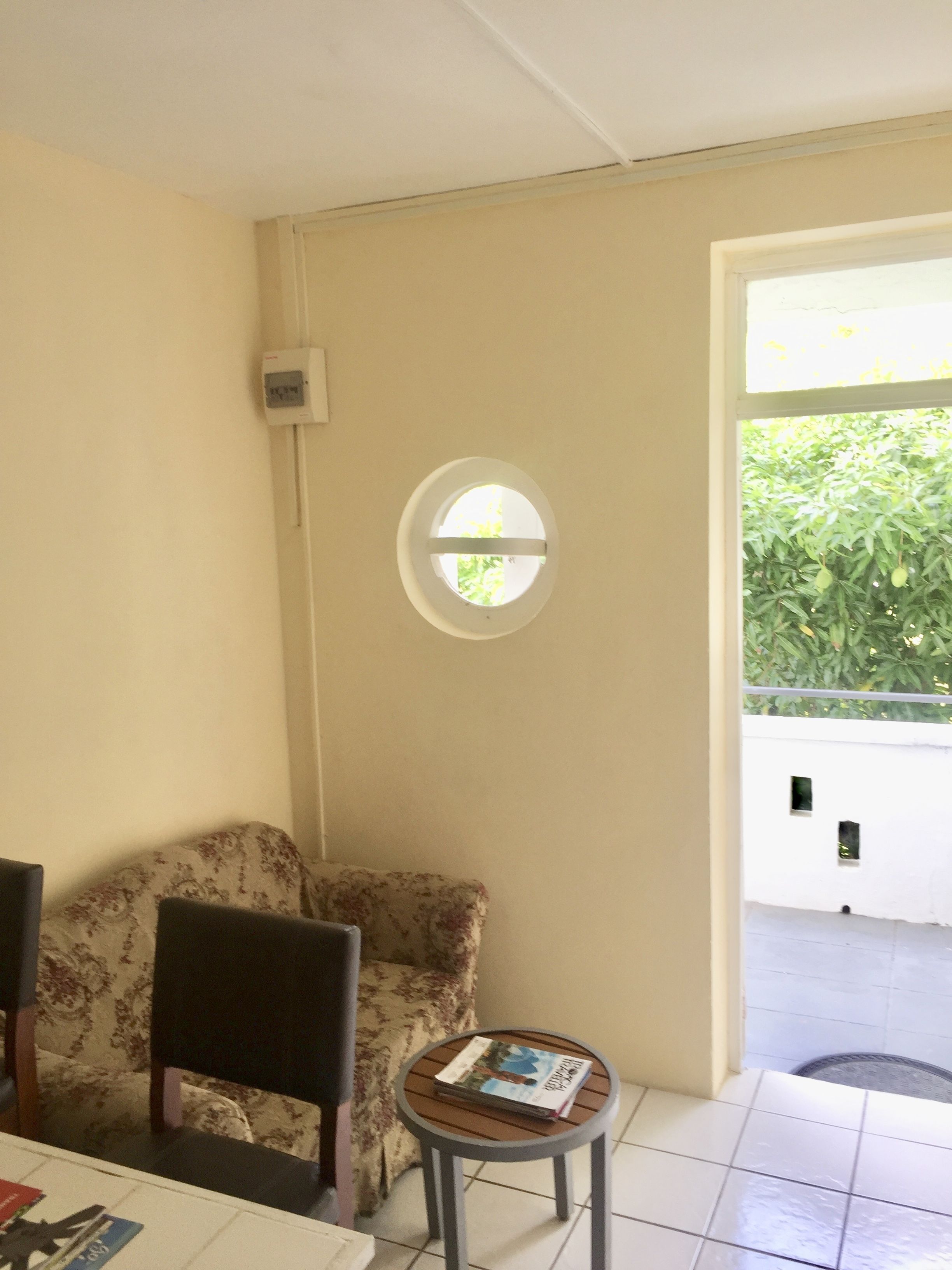 A room with a round table, a floral armchair, a small window, and a door leading outside.