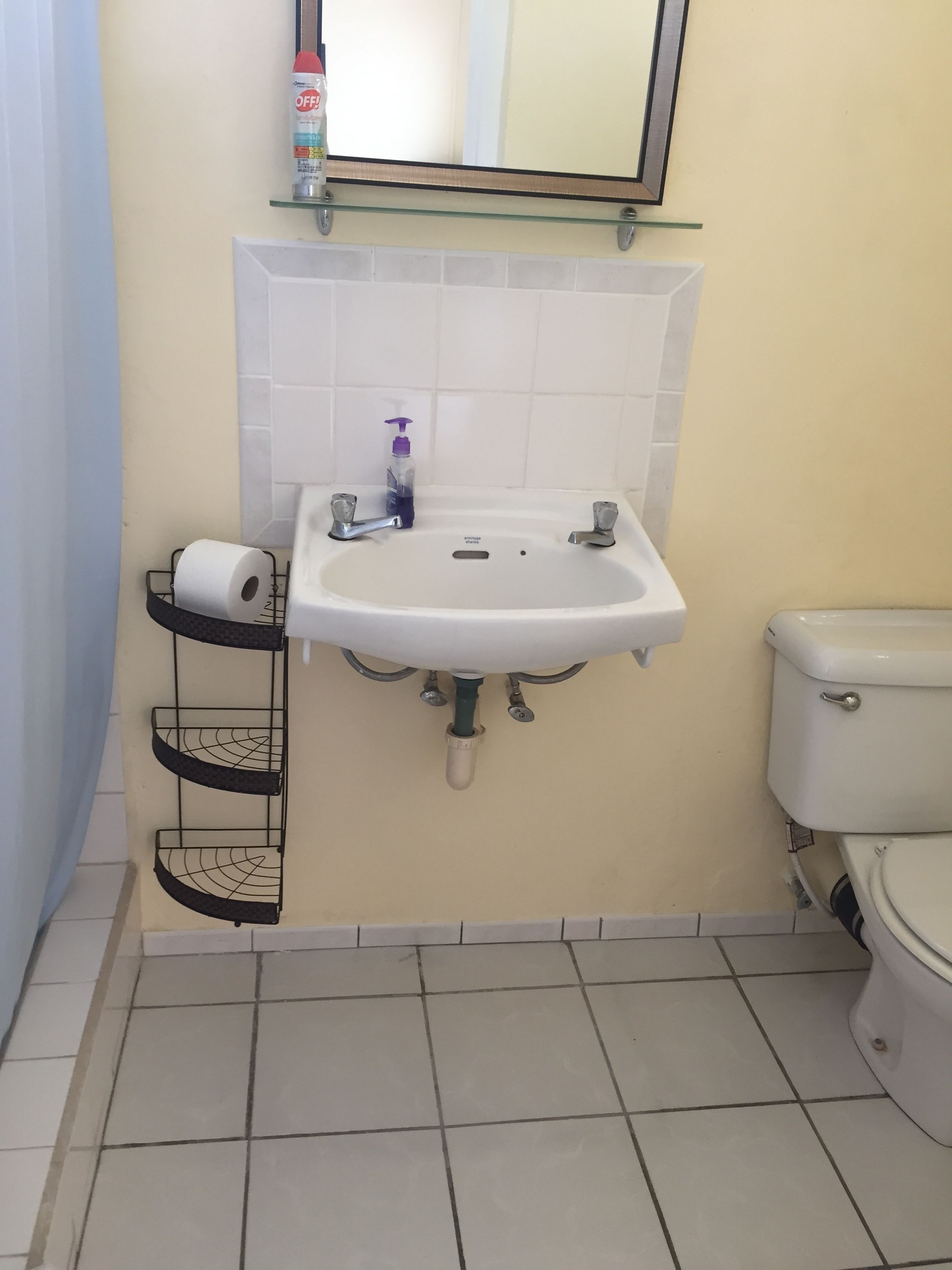 Une salle de bain avec un lavabo blanc, deux robinets, des toilettes et une étagère sur laquelle se trouve un rouleau de papier toilette.