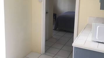 Un couloir étroit avec un lit au fond, une porte blanche et un four à micro-ondes posé sur un comptoir.