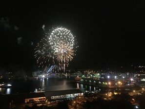 A nighttime view of a waterfront cityscape with fireworks display.
