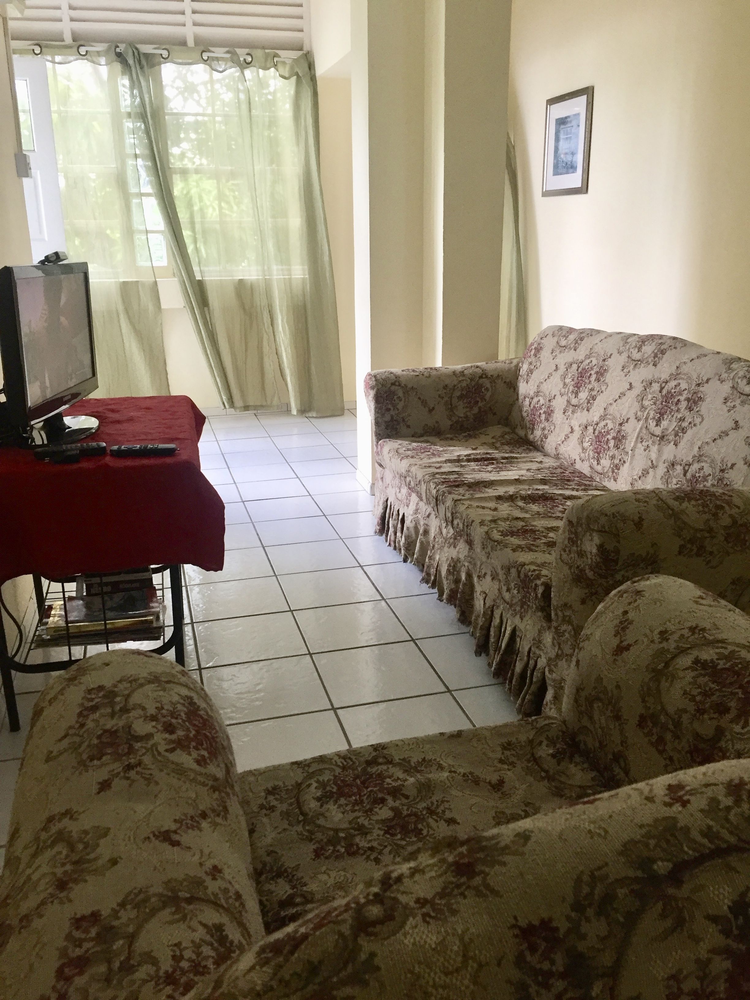 A living room with a sofa, a TV on a stand, and a table with remote controls.