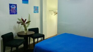 Une pièce comprenant un lit, deux chaises, une petite table avec une plante, et des œuvres d’art murales représentant un voilier, des méduses et une étoile de mer.