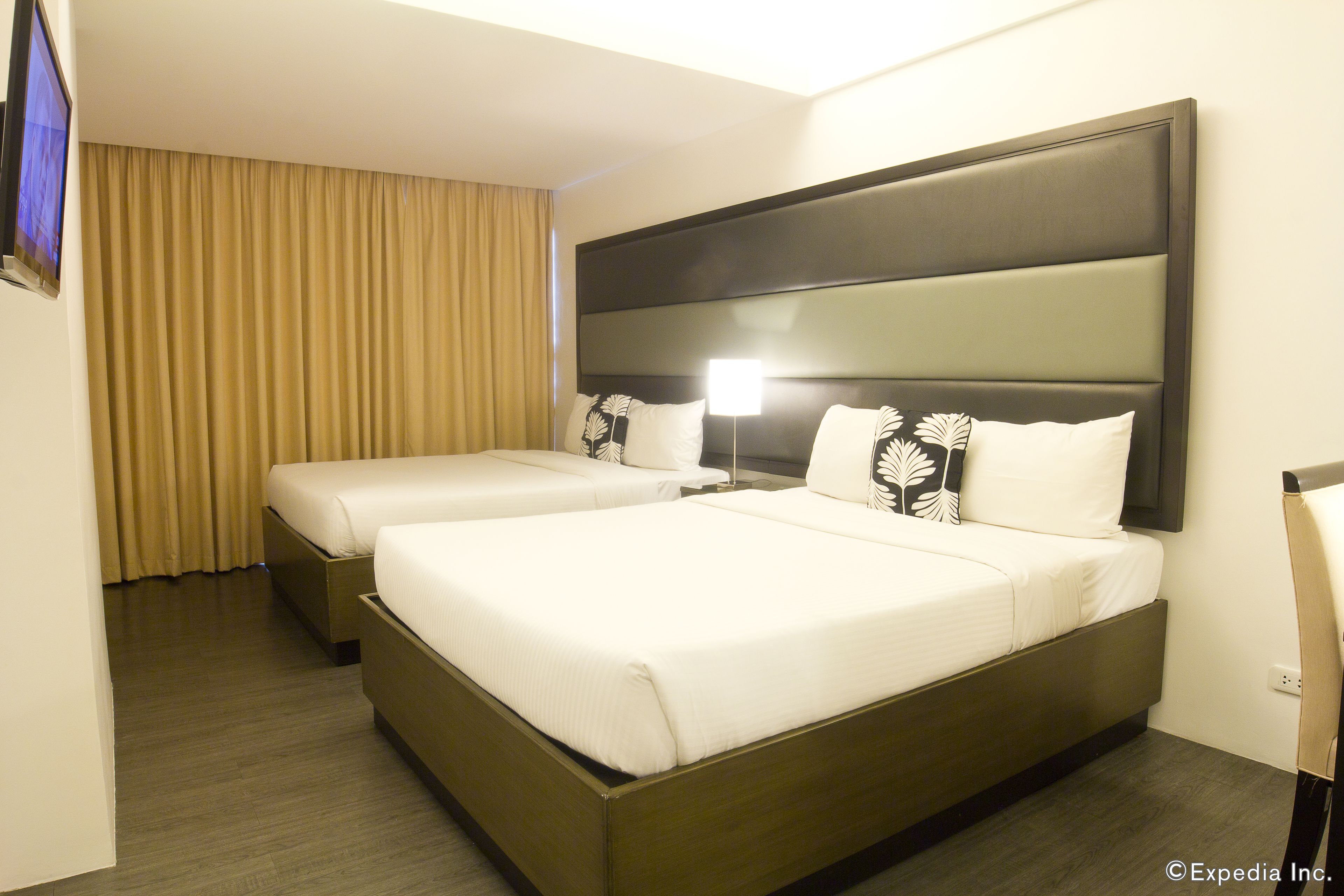 A hotel room with two beds, a flat-screen TV, and a large window with curtains.
