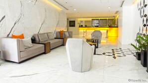 Eine moderne Hotelhalle mit Marmorboden, einer Couch mit orangenen Kissen, einem weißen Sessel und einem Küchenbereich im Hintergrund.