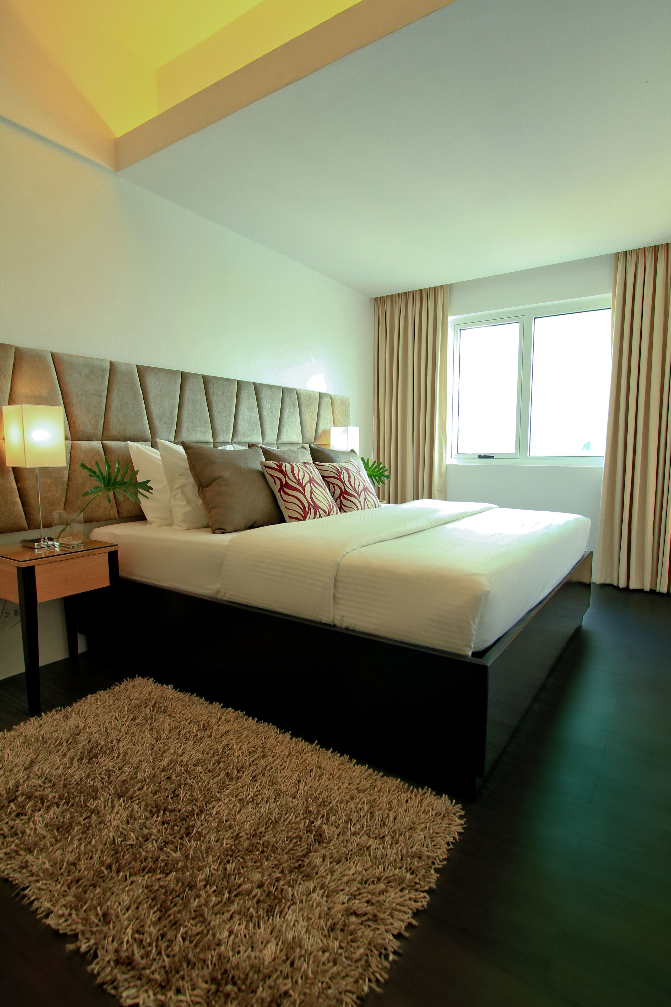 Une chambre à coucher moderne avec un grand lit, une table de chevet, une lampe et une fenêtre avec des rideaux.