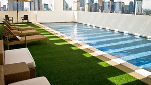 Ein Pool ohne Rand auf dem Dach mit Blick auf die Stadt, Liegestühlen und einem Sonnenschirm.