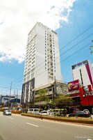 A tall hotel with multiple floors and balconies, surrounded by urban infrastructure and parked cars.