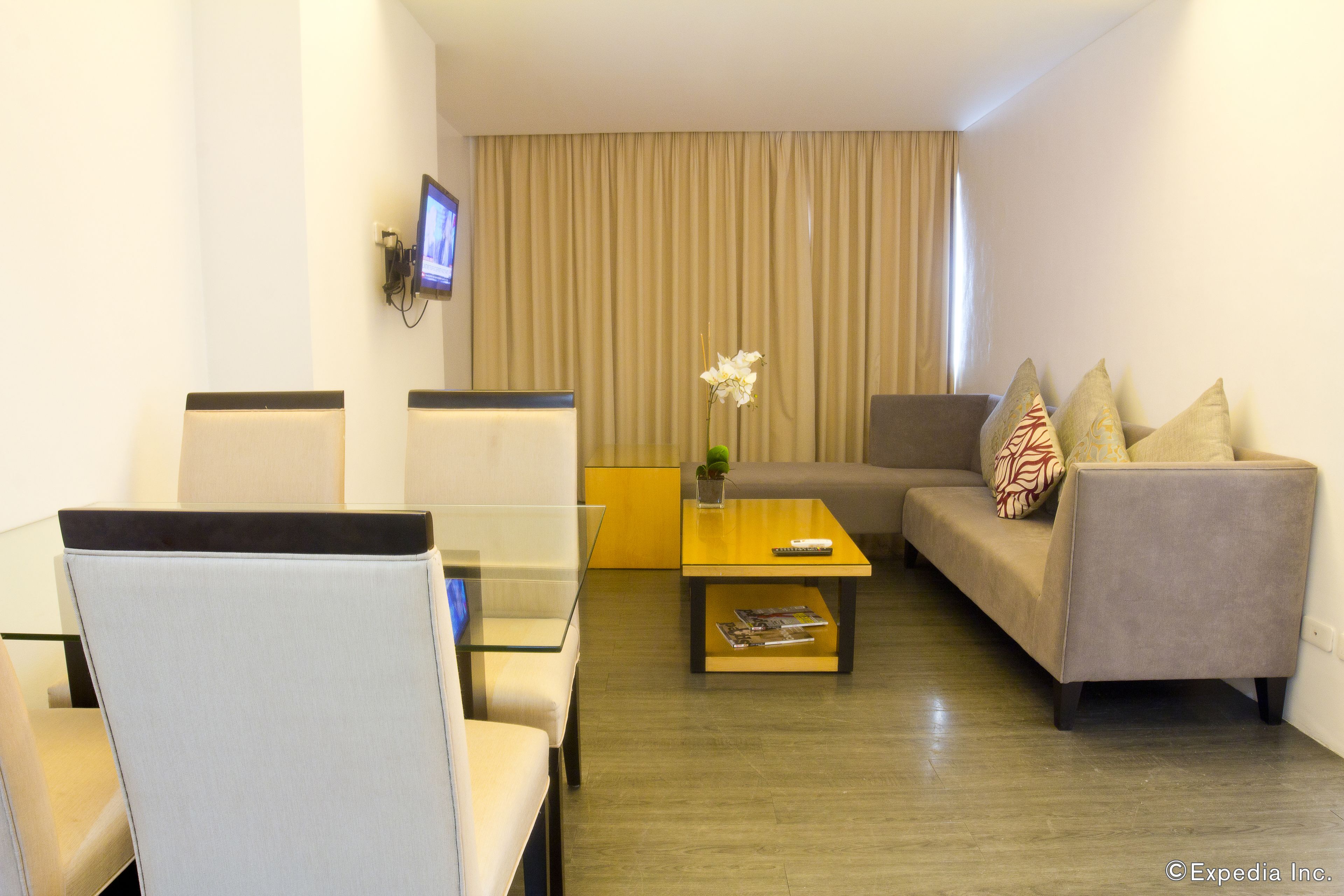 A modern hotel room with a sofa, two armchairs, a coffee table, and a TV mounted on the wall.