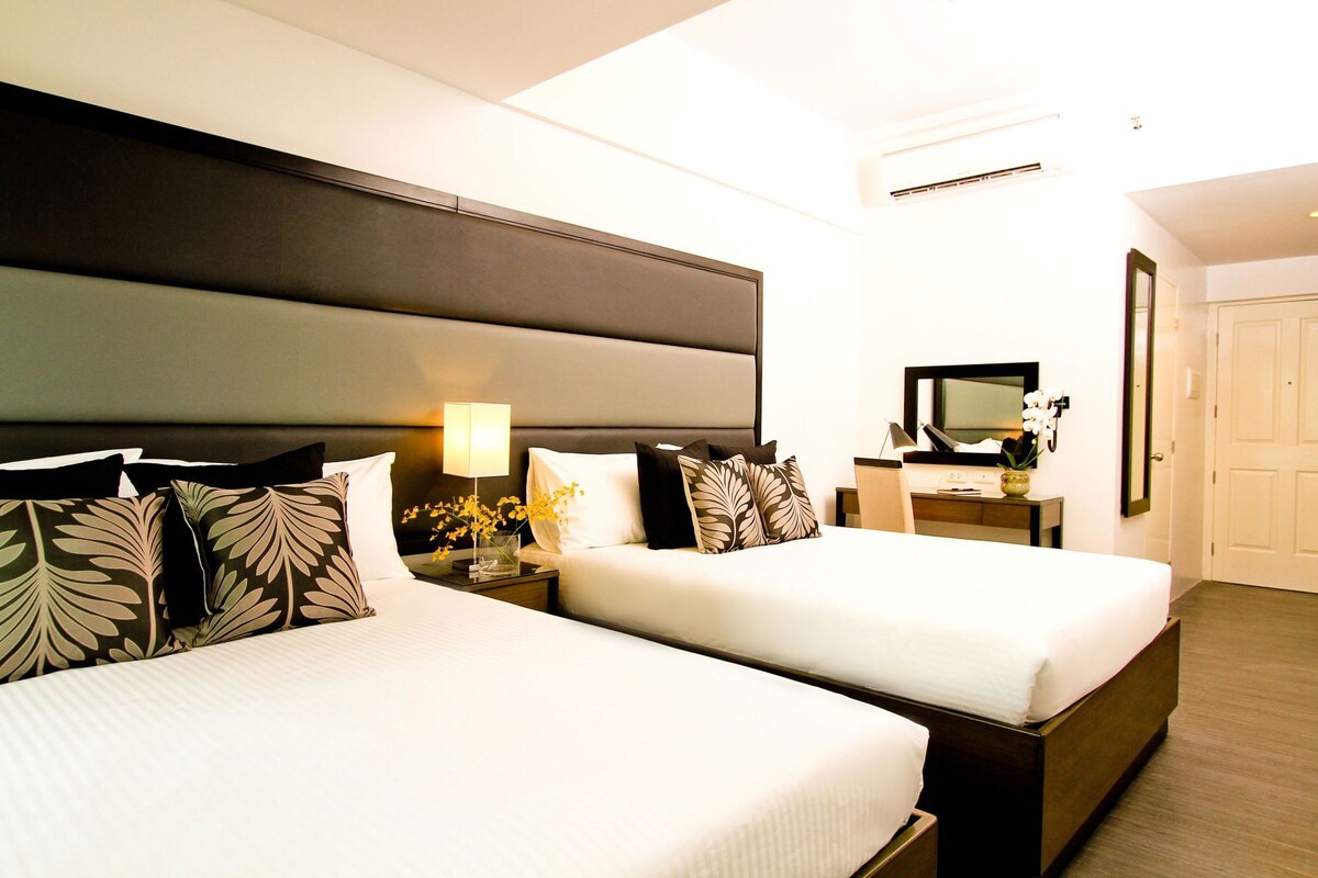 Een hotelkamer met twee bedden, een nachtkastje met lamp, een bureau met computer, een spiegel en een airconditioning.