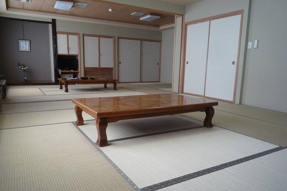 Ein Raum mit Tatami-Matten, einem Holztisch, einer Bank und einer Schiebetür.