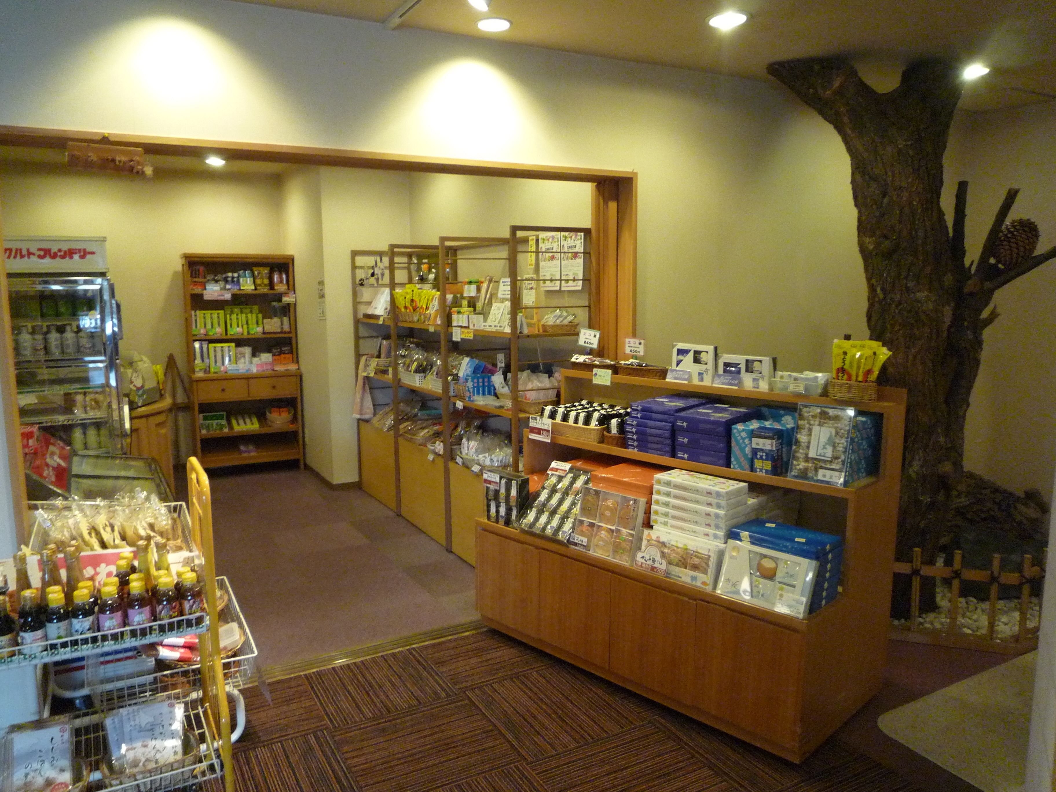 A store with shelves stocked with various products, a display counter, and a decorative tree.