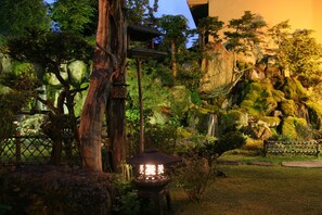 A serene garden with a traditional Japanese lantern, a wooden fence, and a waterfall. - Ryokan Sensyoen (Asahikawa)