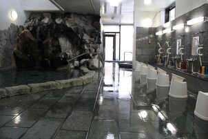 A public restroom with a stone wall, multiple urinals, and a tiled floor.