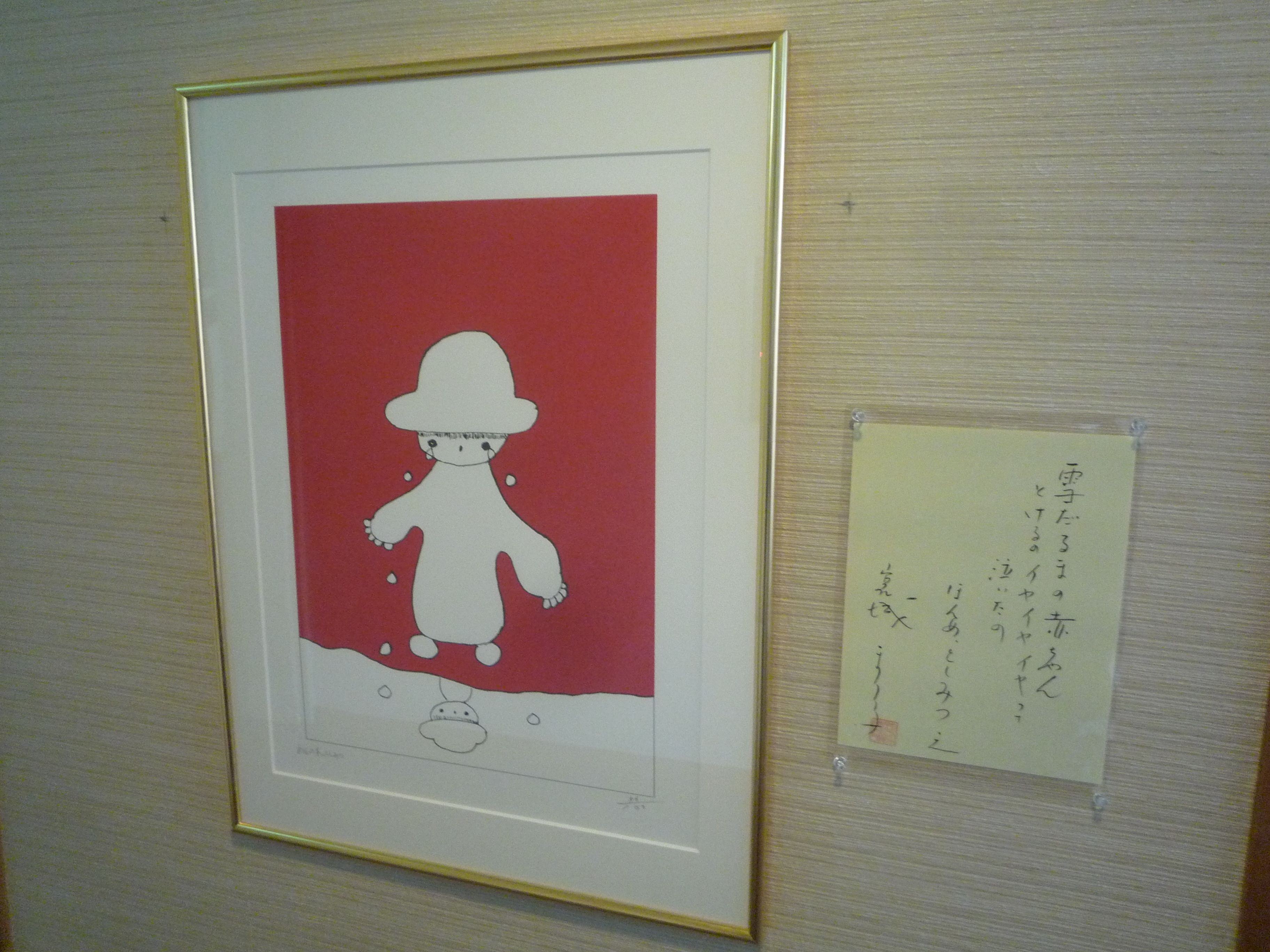 Uma obra de arte emoldurada com fundo vermelho e uma figura branca, possivelmente uma boneca, com chapéu e um objeto pequeno abaixo.