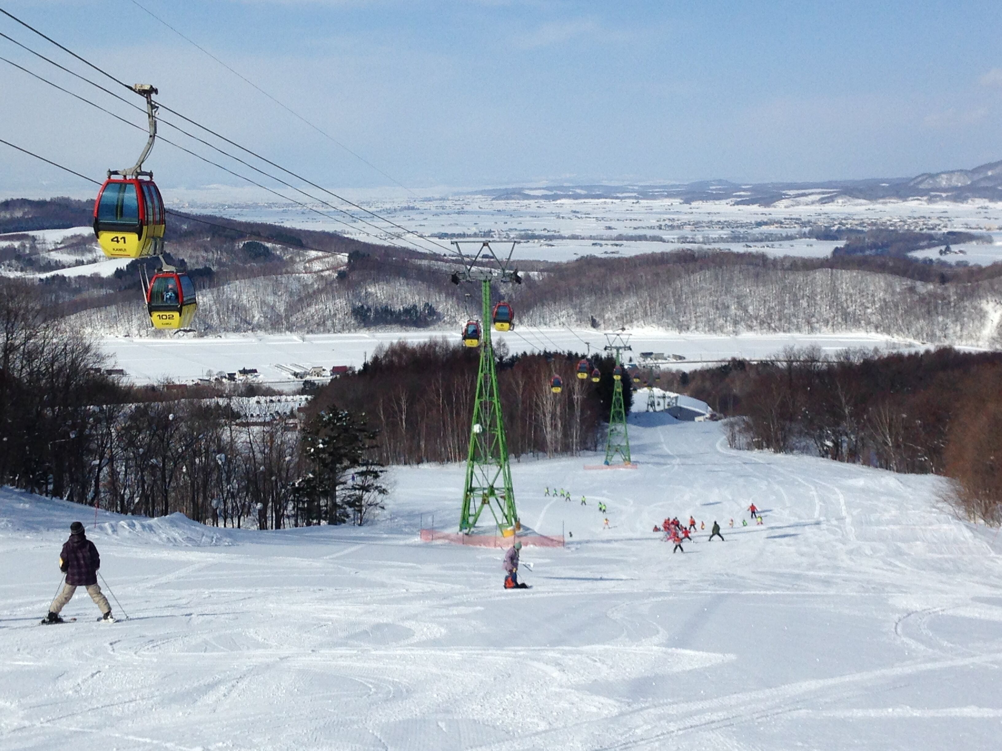 A ski lift with cabins and a chairlift, surrounded by snow-covered terrain and trees.