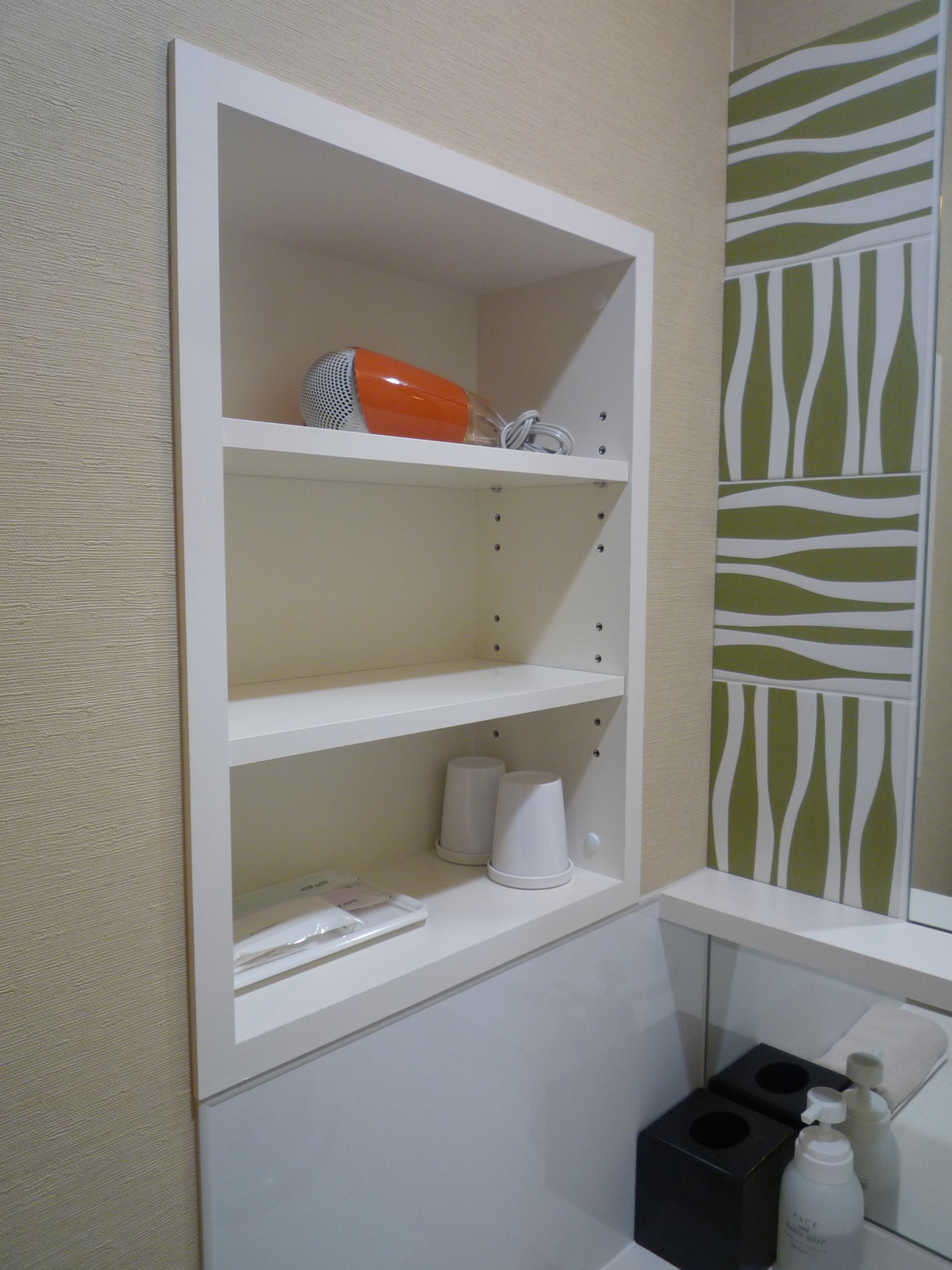 A bathroom with a white shelf unit containing toiletries, a zebra-patterned wall, and a mirror reflecting a towel and soap dispenser.