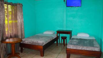 A room with two single beds, a small wooden table, a TV mounted on the wall, and a curtain partially drawn to the side.