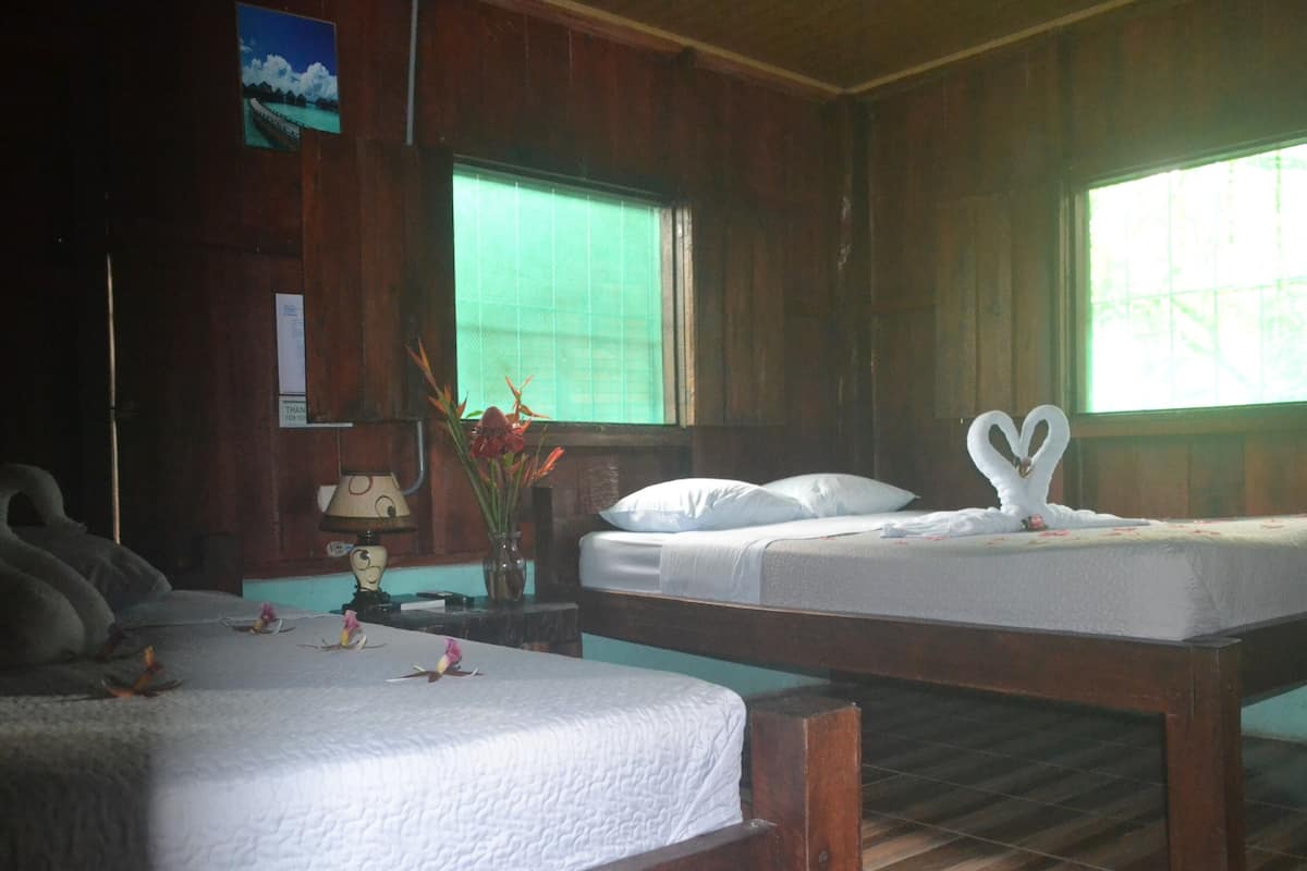 A room with two beds, a lamp, a vase with flowers, and a picture on the wall.