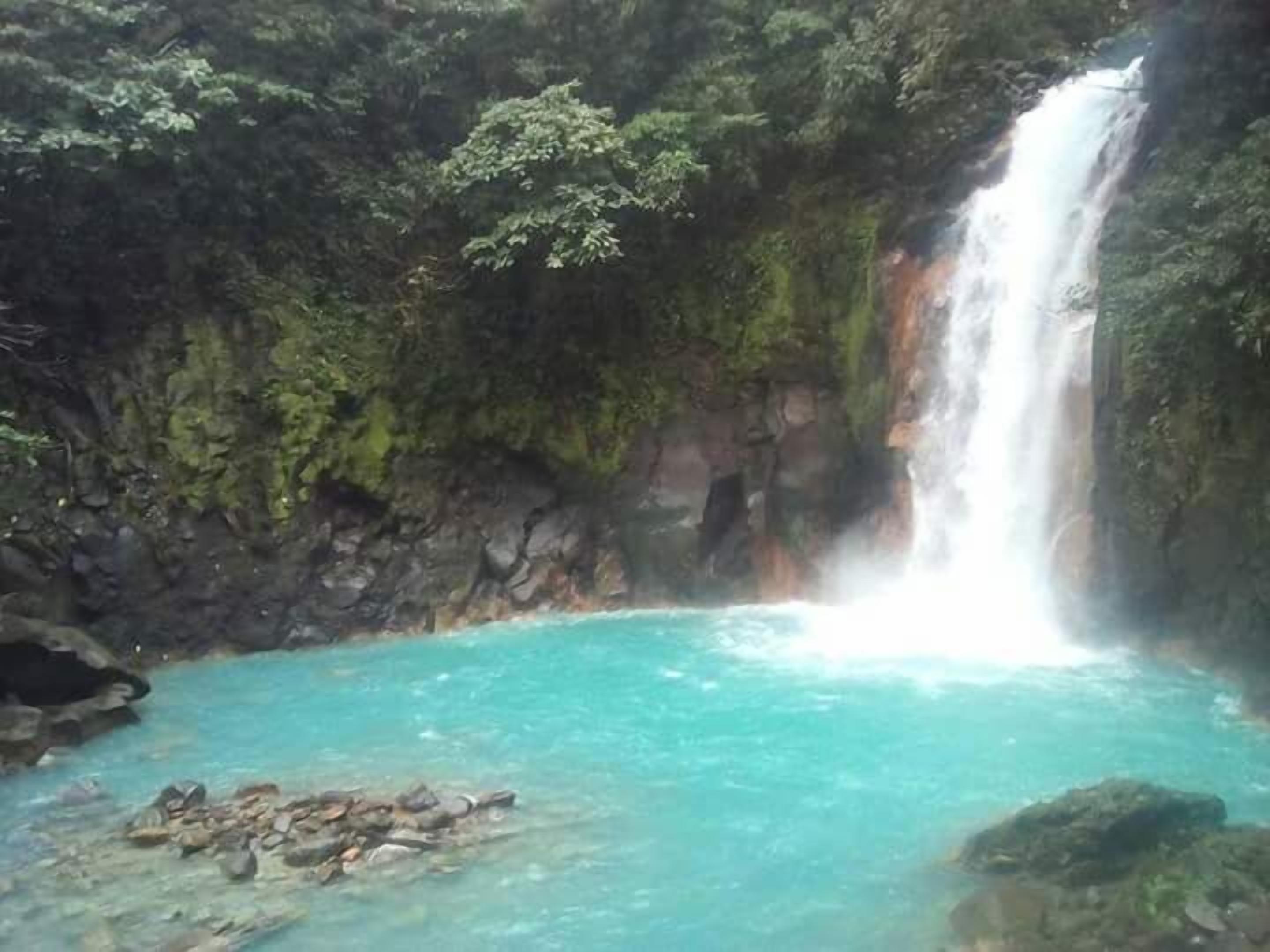 A waterfall cascading into a turquoise pool surrounded by rocky terrain and dense greenery.