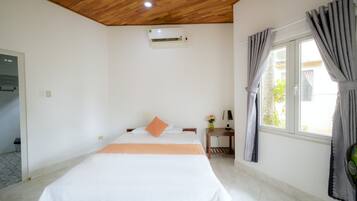 A bedroom with a wooden ceiling, a bed with white and orange bedding, a bedside table with a lamp, and a window with curtains.