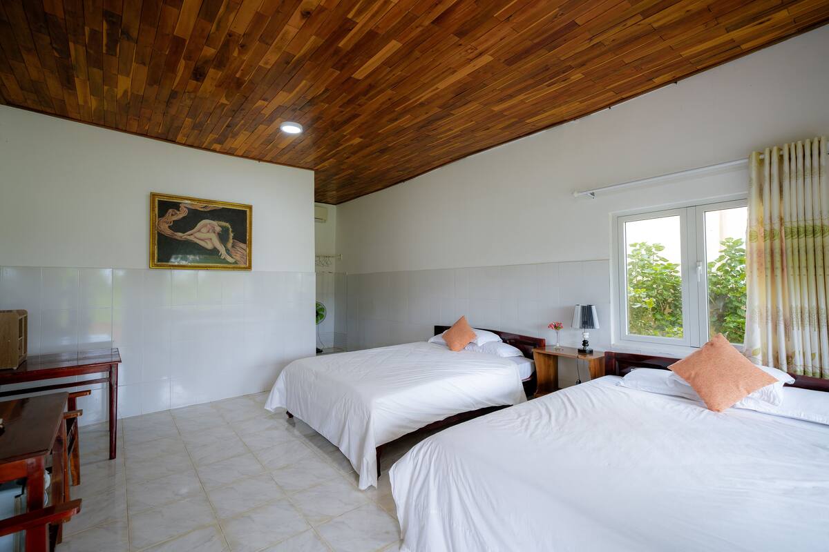 Ein Zimmer mit zwei Betten, einer Holzbalkendecke, einem Bild an der Wand und einem Fenster mit Vorhängen.