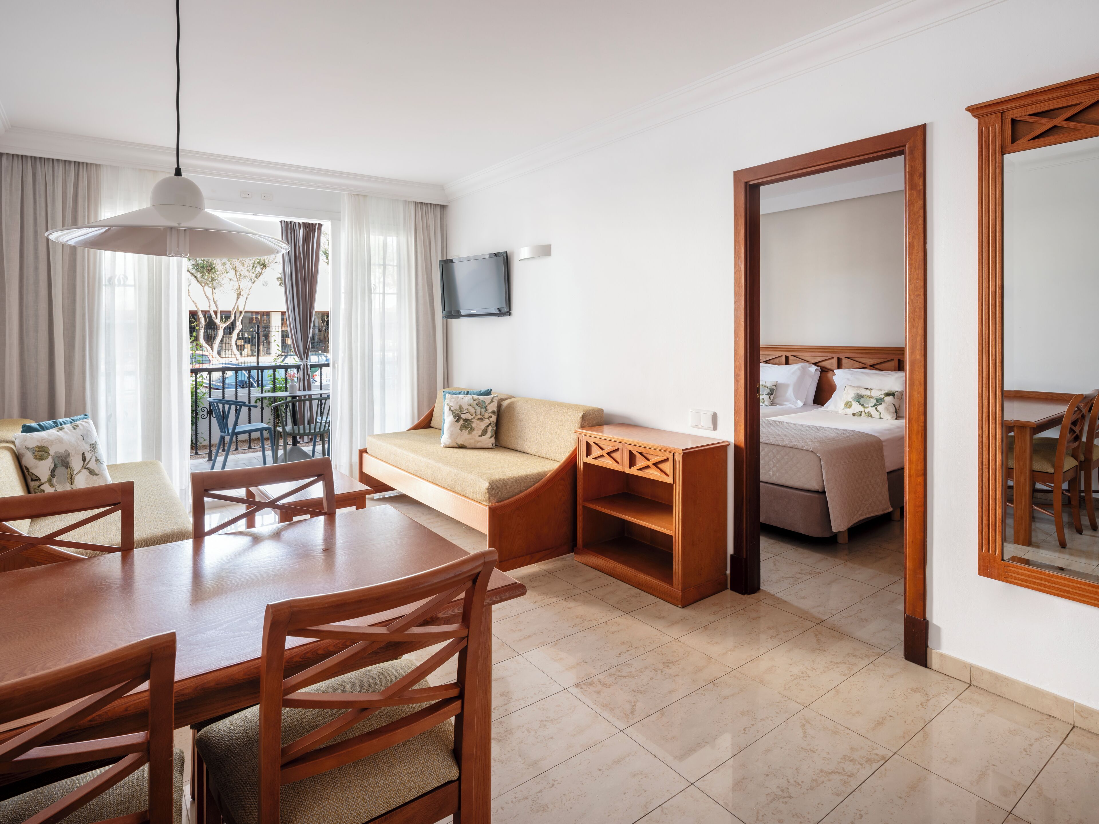 A modern hotel room with a dining area, a sofa, a bed, and a TV.
