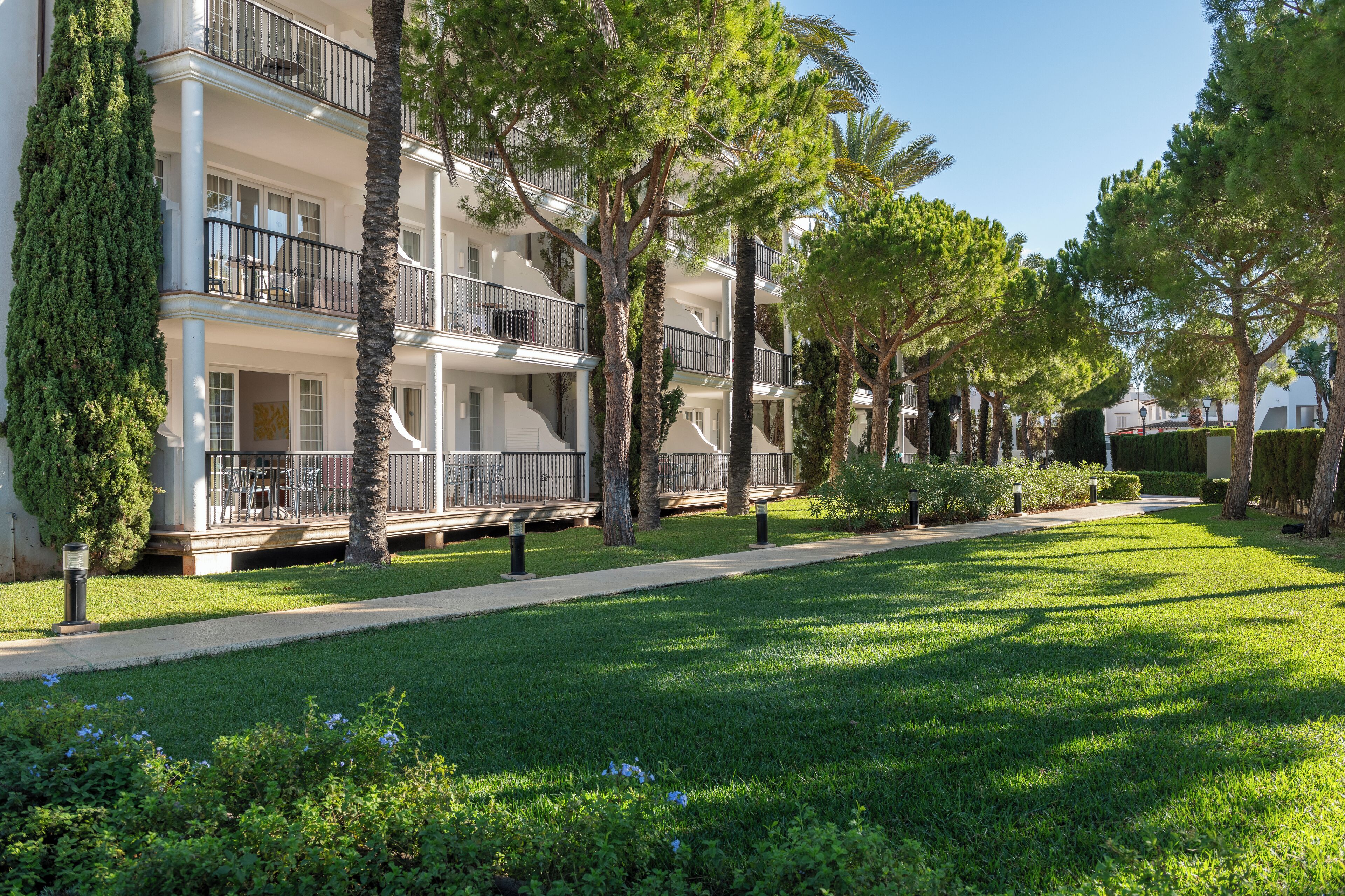 A multi-story hotel with balconies, surrounded by well-maintained lawns and trees.